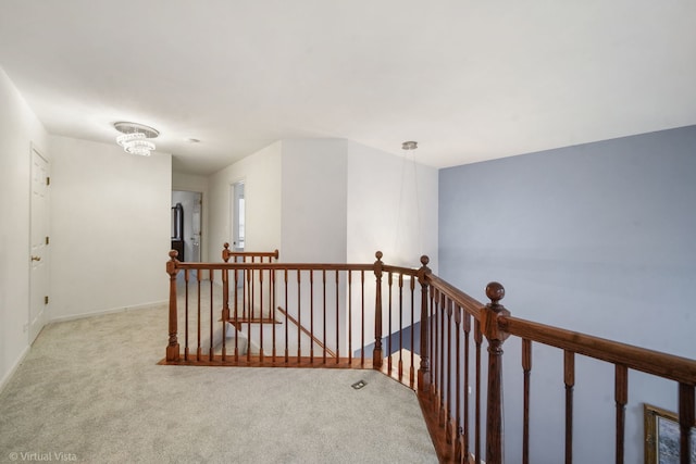 hall with carpet floors, baseboards, a notable chandelier, and an upstairs landing