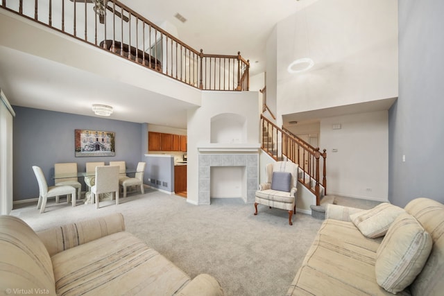 carpeted living area with a fireplace, visible vents, a towering ceiling, stairs, and baseboards