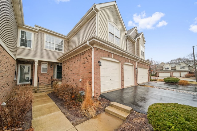 townhome / multi-family property featuring a garage, driveway, and brick siding