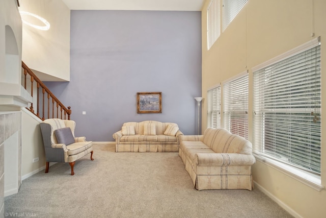 carpeted living area with stairway, a towering ceiling, and baseboards