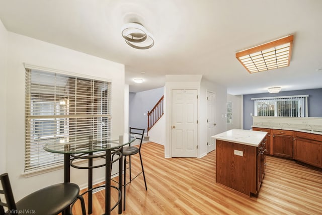 kitchen with light stone counters, brown cabinets, a sink, light wood-type flooring, and baseboards