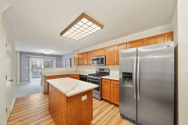 kitchen featuring a kitchen island, appliances with stainless steel finishes, a peninsula, light wood-type flooring, and a sink