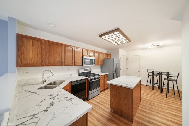 kitchen with a kitchen island, appliances with stainless steel finishes, light stone counters, light wood-type flooring, and a sink