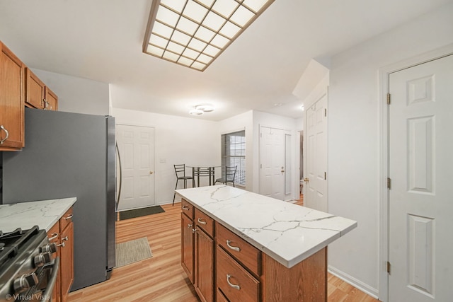 kitchen with brown cabinetry, light wood-style flooring, a kitchen island, appliances with stainless steel finishes, and light stone counters