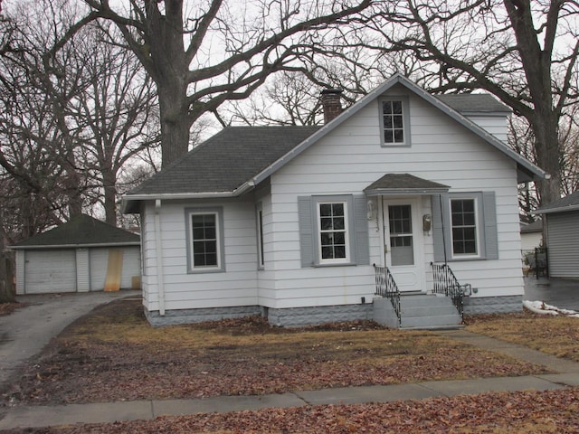 bungalow-style house with a garage, a shingled roof, a chimney, and an outdoor structure