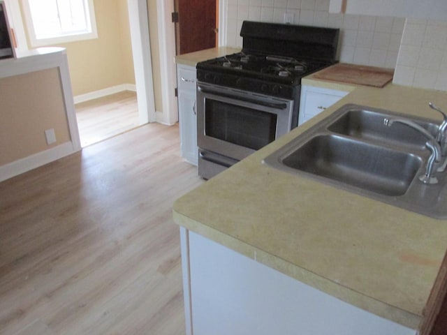 kitchen with light wood-type flooring, stainless steel range with gas stovetop, a sink, and backsplash