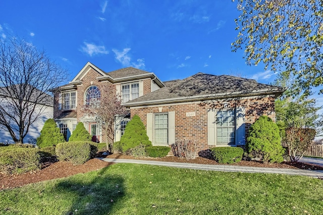 view of front of property featuring a front yard, brick siding, and roof with shingles