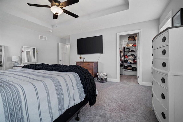 carpeted bedroom featuring baseboards, visible vents, a closet, a walk in closet, and a raised ceiling