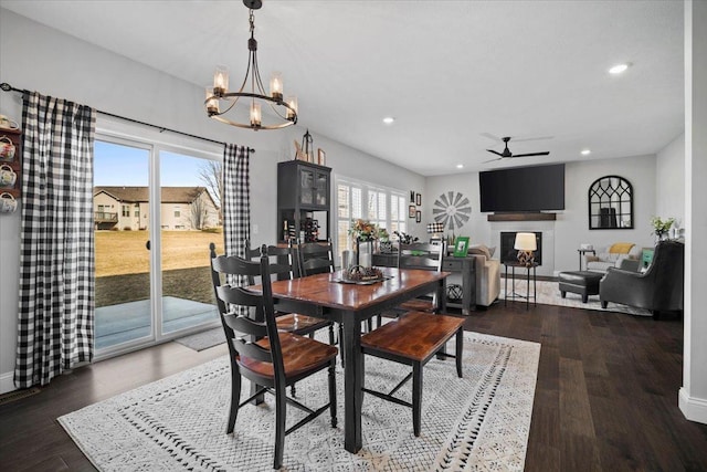 dining room with baseboards, recessed lighting, ceiling fan with notable chandelier, a fireplace, and wood finished floors