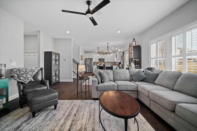 living area with ceiling fan with notable chandelier, stairway, wood finished floors, and baseboards