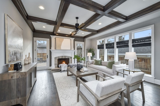 living room with beamed ceiling, coffered ceiling, a stone fireplace, and a ceiling fan