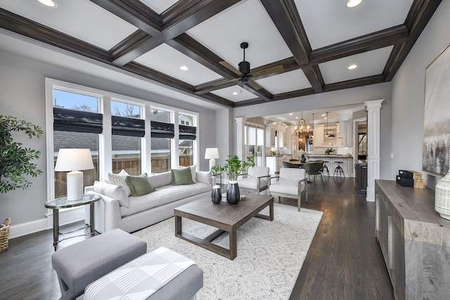 living area featuring beamed ceiling, decorative columns, ceiling fan with notable chandelier, and coffered ceiling