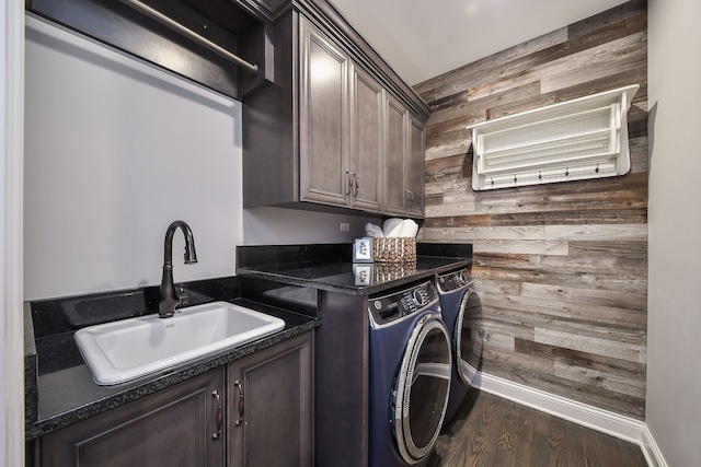 clothes washing area with a sink, washing machine and dryer, wood finished floors, cabinet space, and wood walls