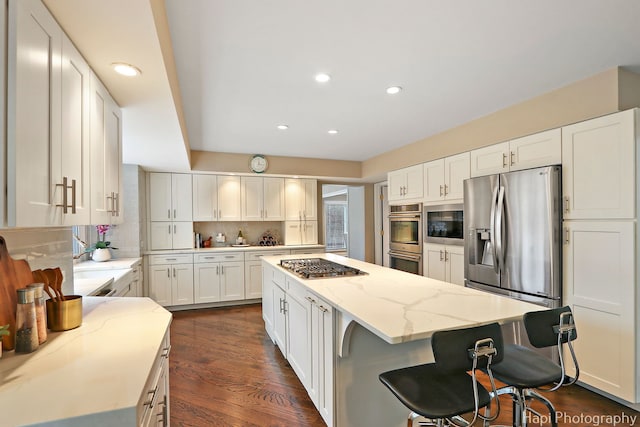 kitchen featuring backsplash, a kitchen island, stainless steel appliances, white cabinets, and light stone countertops