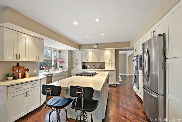 kitchen featuring a breakfast bar, light stone counters, dark wood finished floors, a center island, and appliances with stainless steel finishes