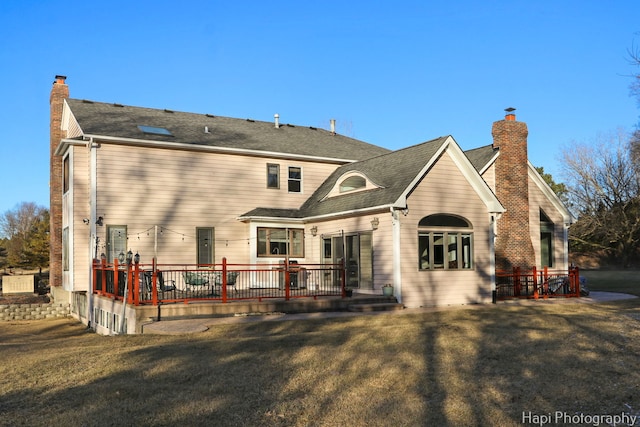 back of property featuring a lawn, a deck, a chimney, and a shingled roof