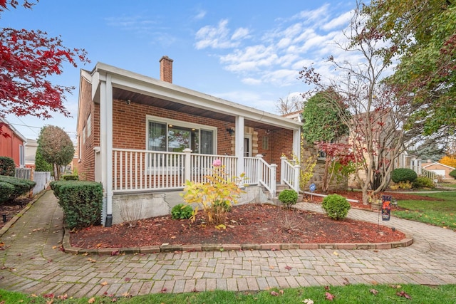 view of front facade featuring covered porch, brick siding, and a chimney