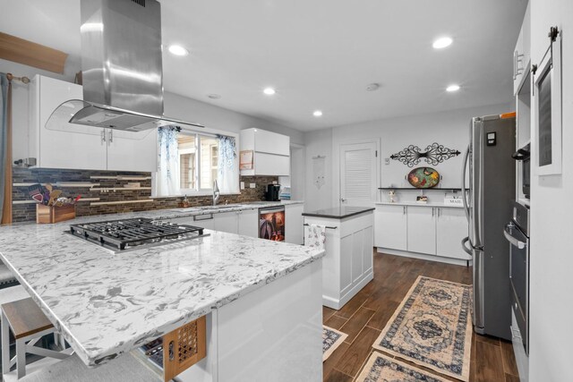 kitchen with stainless steel appliances, dark wood-type flooring, a peninsula, white cabinetry, and island exhaust hood