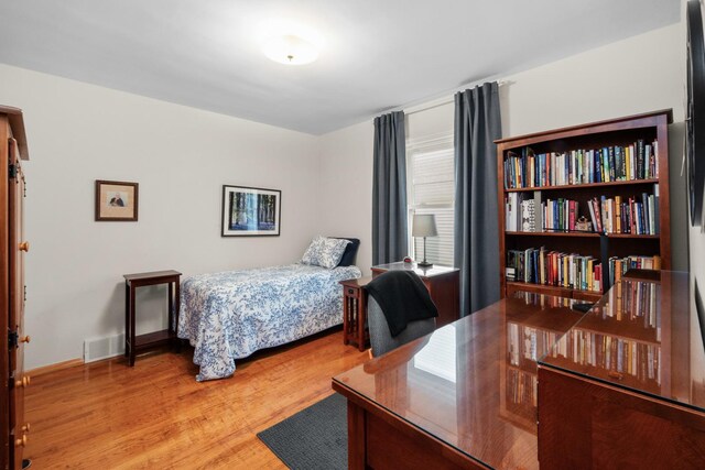 bedroom with baseboards, visible vents, and wood finished floors