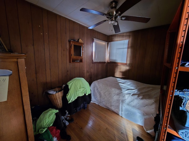 bedroom with ceiling fan, wood walls, and wood finished floors