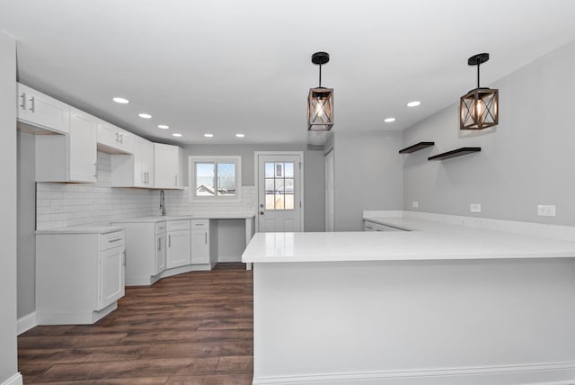 kitchen with dark wood-style floors, pendant lighting, backsplash, white cabinets, and a peninsula