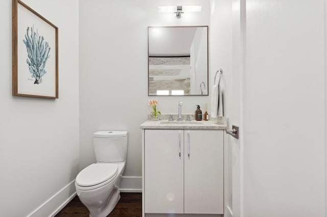 bathroom with toilet, vanity, baseboards, and wood finished floors