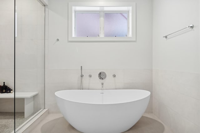 bathroom featuring tile walls, a walk in shower, and a freestanding bath