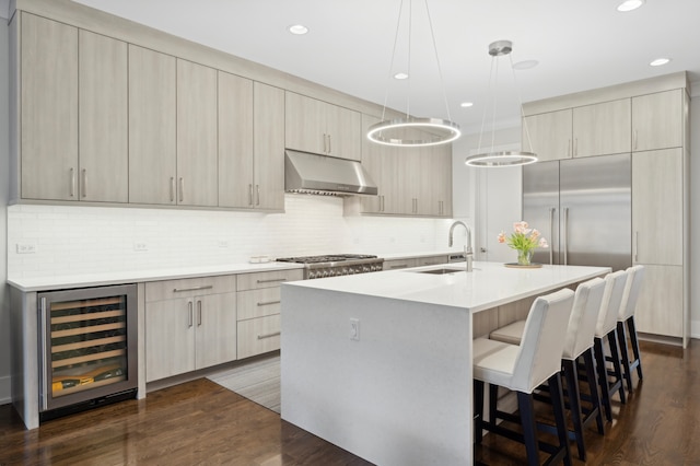 kitchen with beverage cooler, a center island with sink, under cabinet range hood, a sink, and a kitchen breakfast bar