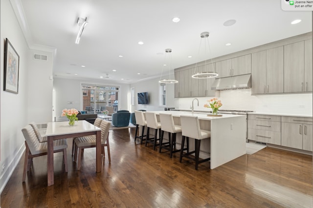 kitchen with visible vents, modern cabinets, a breakfast bar, a center island with sink, and under cabinet range hood