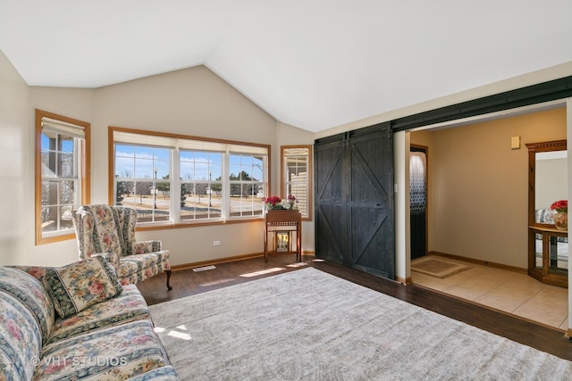 living area featuring lofted ceiling, wood finished floors, baseboards, and a barn door