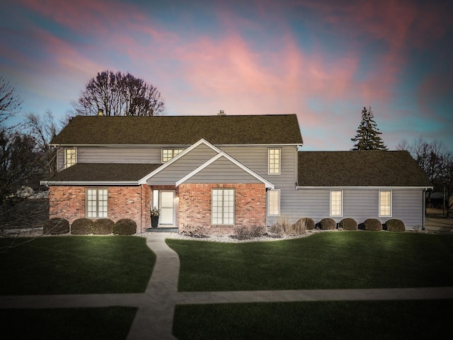 traditional-style home featuring brick siding, roof with shingles, and a front lawn