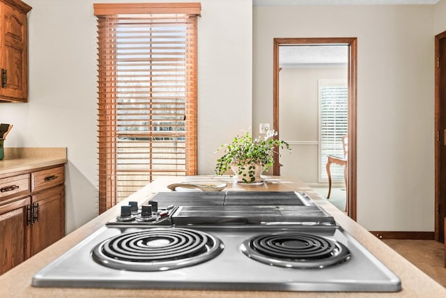 details with light countertops, brown cabinetry, baseboards, and stovetop with downdraft