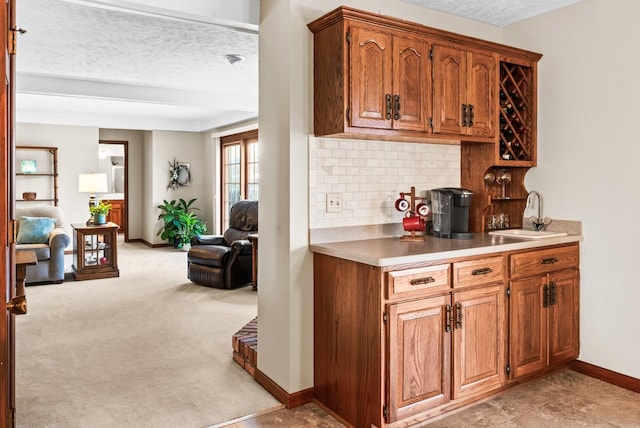 kitchen with backsplash, light carpet, brown cabinetry, a textured ceiling, and a sink