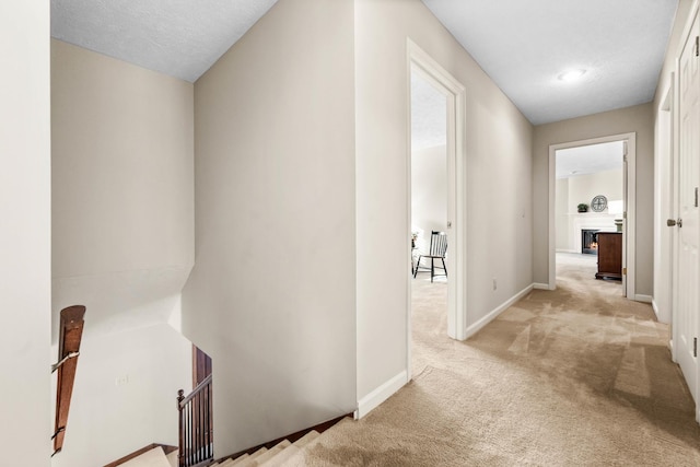 corridor featuring baseboards, light carpet, and an upstairs landing