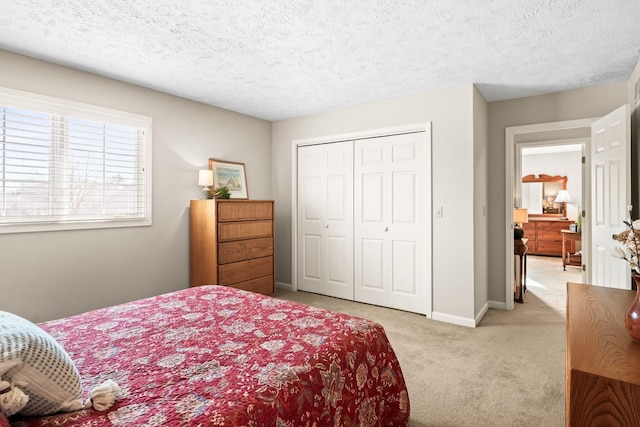 bedroom featuring a textured ceiling, baseboards, a closet, and light carpet