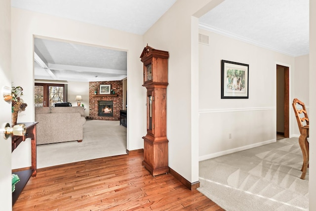 hallway featuring wood finished floors, visible vents, baseboards, beam ceiling, and ornamental molding