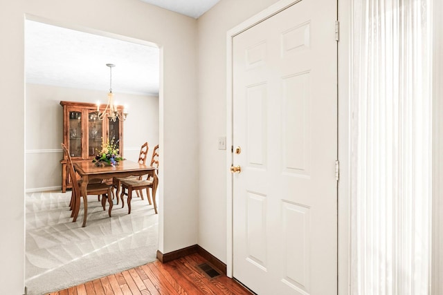 foyer entrance with a chandelier, visible vents, baseboards, and wood finished floors