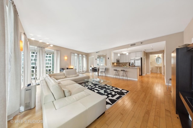 living room featuring light wood-style floors, baseboards, and visible vents