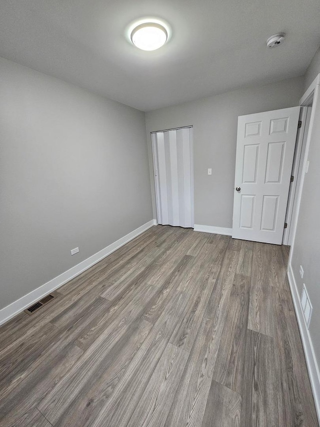 unfurnished bedroom with a closet, visible vents, baseboards, and wood finished floors