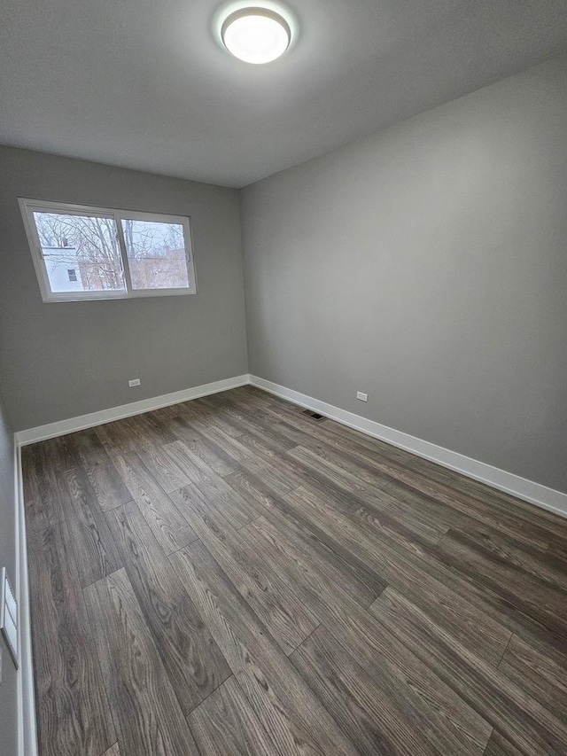 spare room with dark wood-style flooring, visible vents, and baseboards