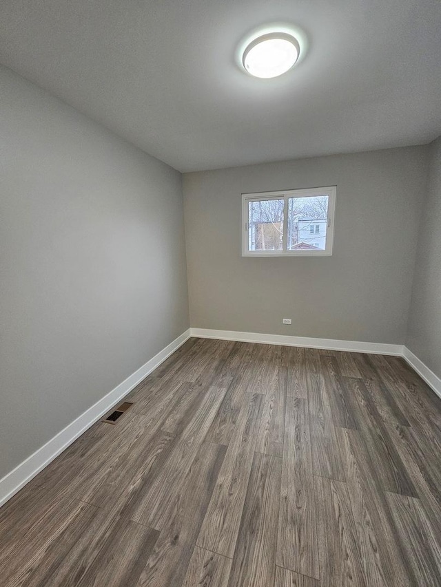 unfurnished room with baseboards, visible vents, and dark wood finished floors