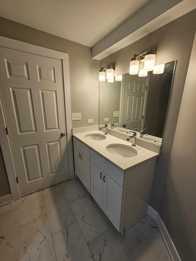 full bathroom with double vanity, marble finish floor, baseboards, and a sink