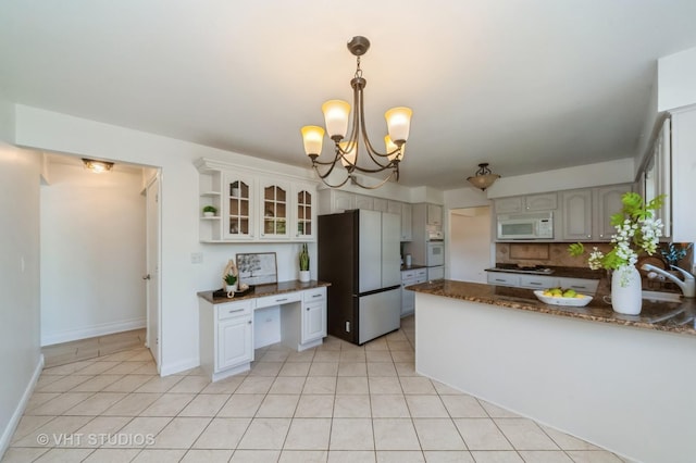 kitchen featuring light tile patterned floors, white microwave, oven, a peninsula, and freestanding refrigerator