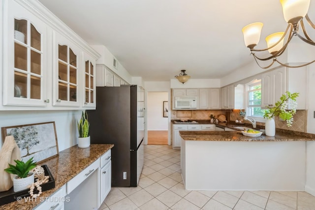 kitchen with white microwave, a sink, freestanding refrigerator, tasteful backsplash, and glass insert cabinets