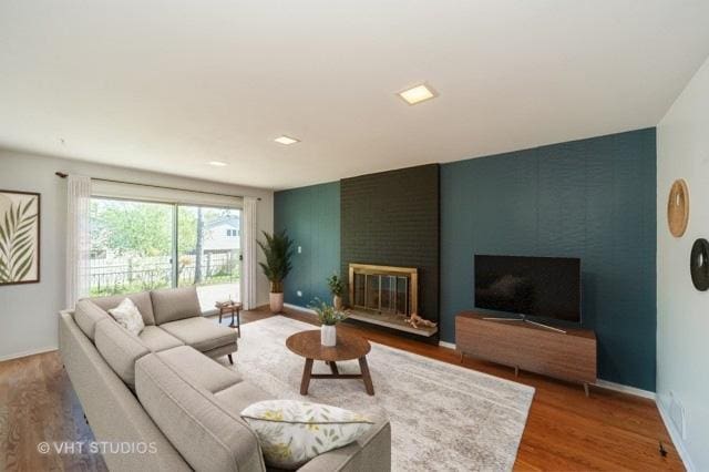 living room with a brick fireplace, baseboards, and wood finished floors