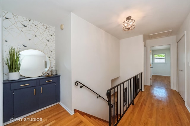 hall with an upstairs landing, attic access, baseboards, and light wood finished floors