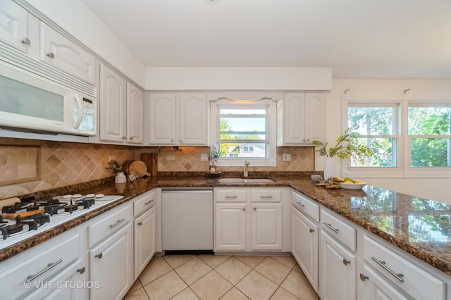 kitchen featuring white appliances, a sink, white cabinetry, backsplash, and dark stone counters