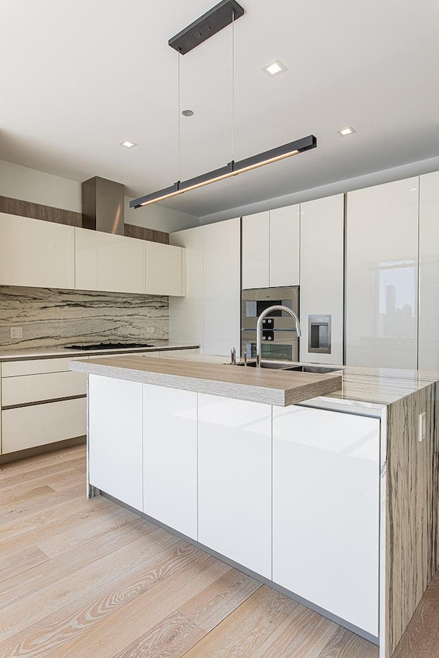 kitchen featuring tasteful backsplash, white cabinets, modern cabinets, light wood-type flooring, and a sink