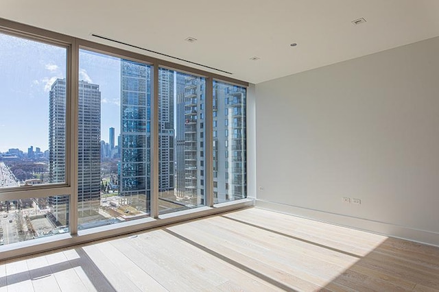 unfurnished room with expansive windows, baseboards, wood finished floors, and a city view