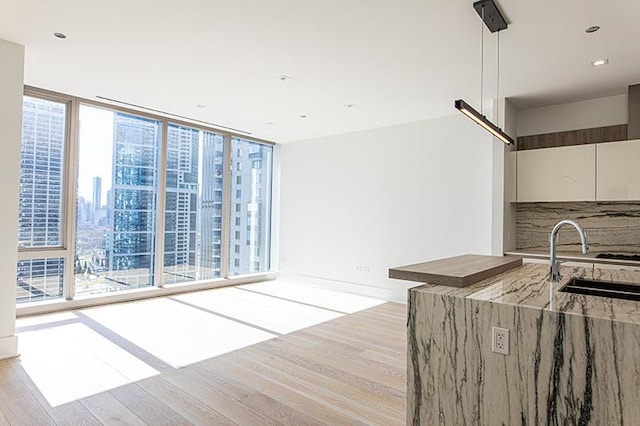 kitchen featuring decorative backsplash, light wood-style flooring, light stone countertops, floor to ceiling windows, and a sink